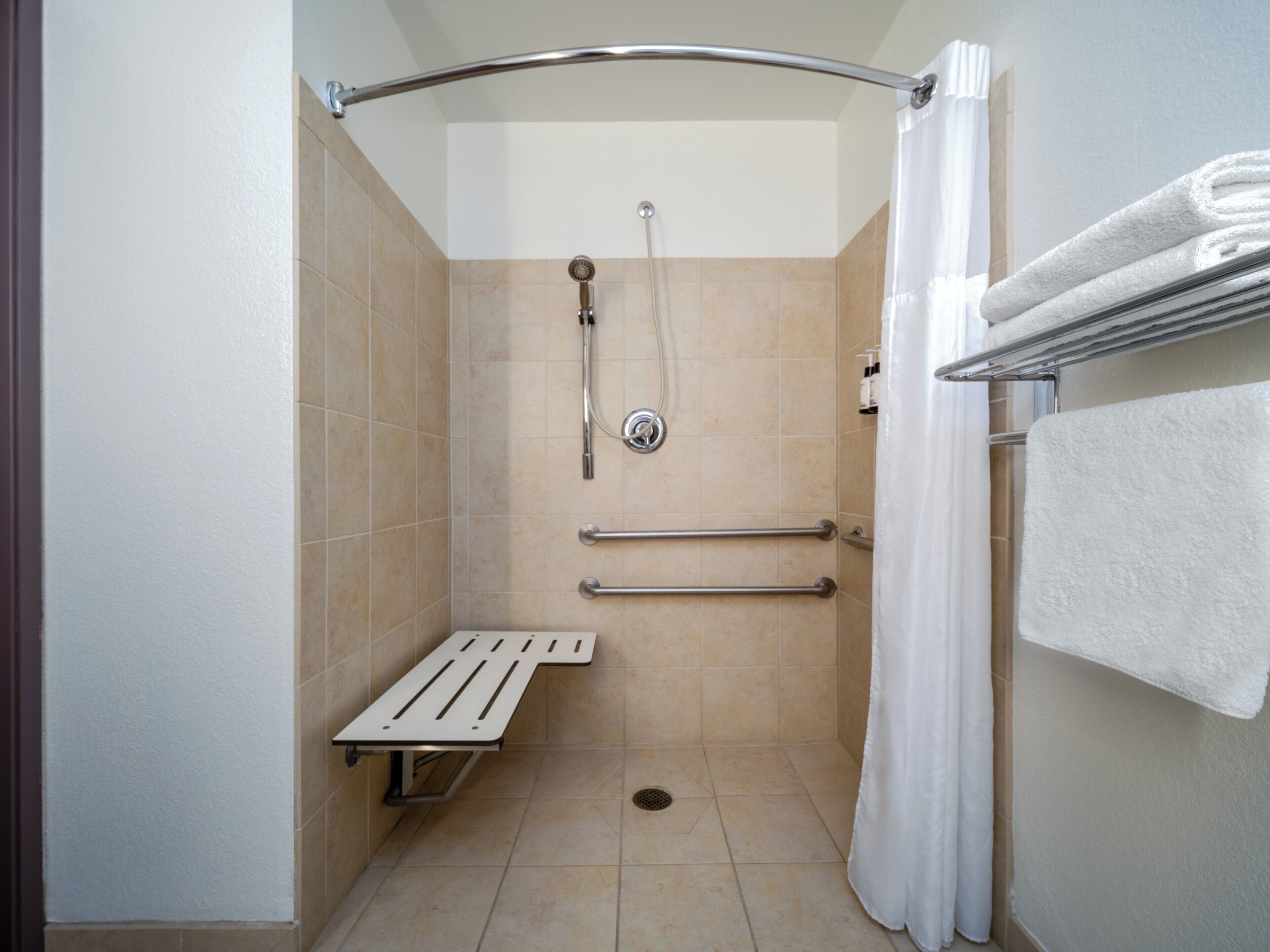 A small, enclosed shower area with a bench, grab bars, and a showerhead.