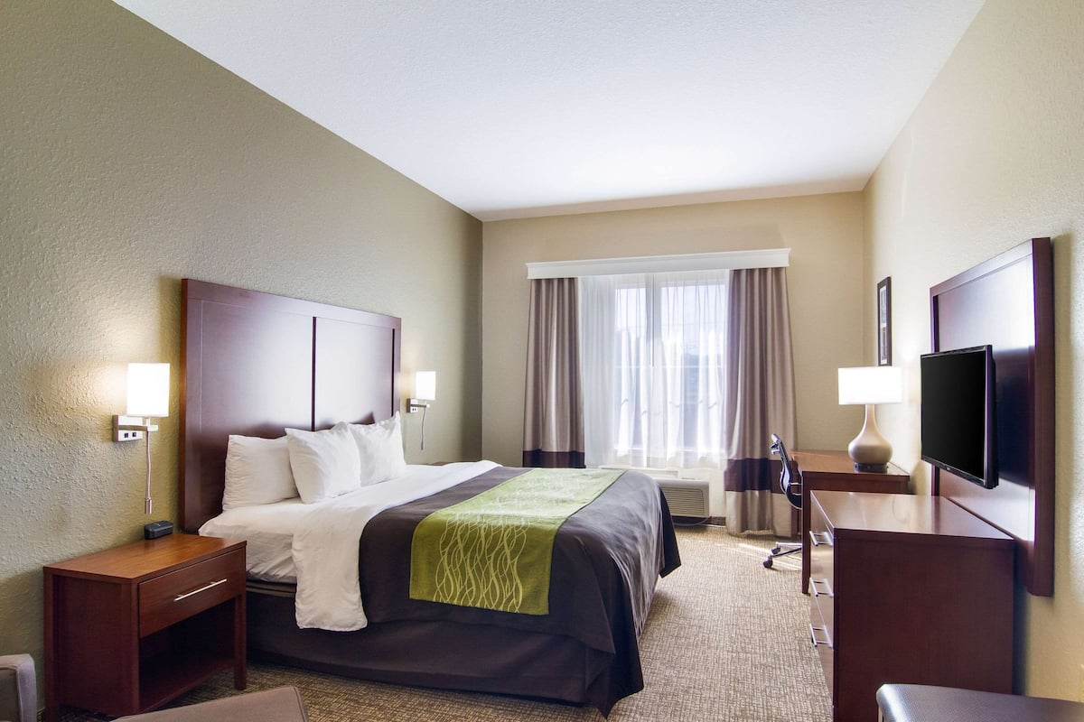 A hotel room with a large bed, bedside tables, a desk with a chair, a flat-screen TV, and a window with curtains.