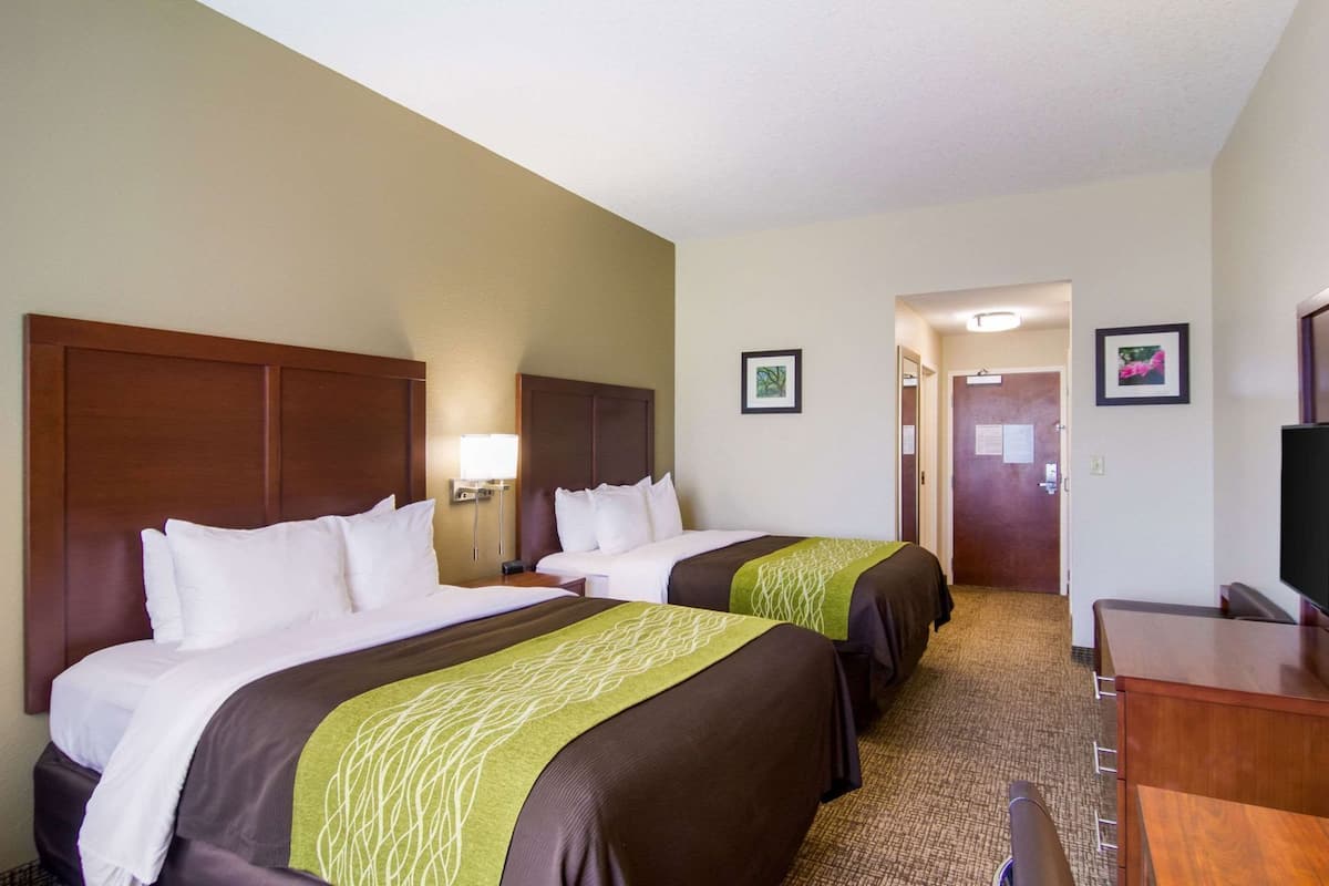 A hotel room with two beds, a desk, a TV, and a door leading to a hallway.