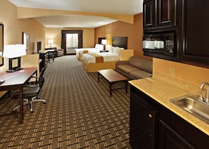 A hotel room with a bed, sofa, desk, and kitchenette.