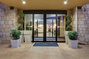 Een hotelentree met een stenen gevel, automatische schuifdeuren en potplanten.