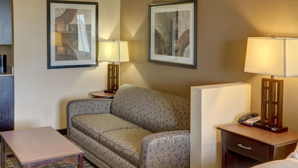 A hotel room with a sofa, a small table, a bedside table with a lamp, a phone, and a framed picture on the wall.