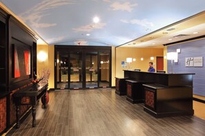Een hotel receptie met een modern design, inclusief een receptiebalie, een digitaal informatiebord en een plafond met een wolkenpatroon.