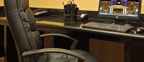 Habitación de hotel con una silla de oficina de cuero negro, un escritorio con computadora, teclado, ratón y una cafetera.