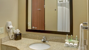 A bathroom with a granite countertop, a white sink, a mirror, a door, and a towel rack.