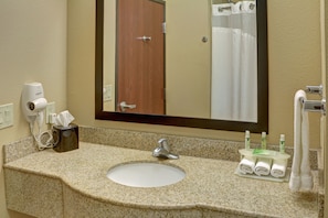 Un baño con encimera de granito, un lavabo blanco, un espejo, una puerta y un perchero para toallas.