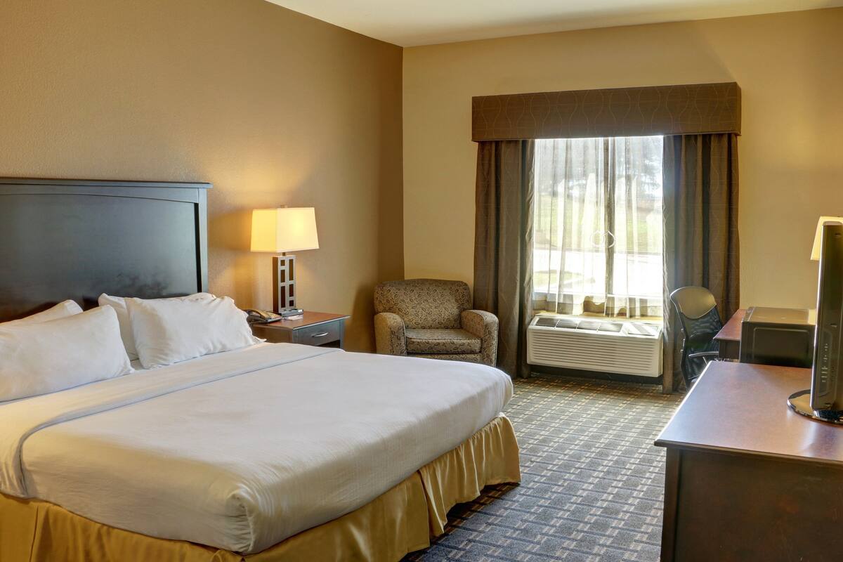 Een hotelkamer met een groot bed, een bureau, een stoel, een lamp en een raam met gordijnen.