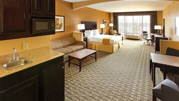 A hotel room with a kitchenette, a sofa, a bed, a desk, and a chair.