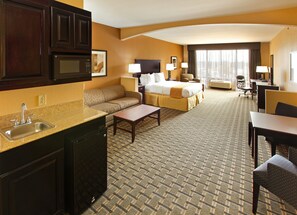 Een hotelkamer met een kitchenette, een slaapbank, een bed, een bureau en een stoel.