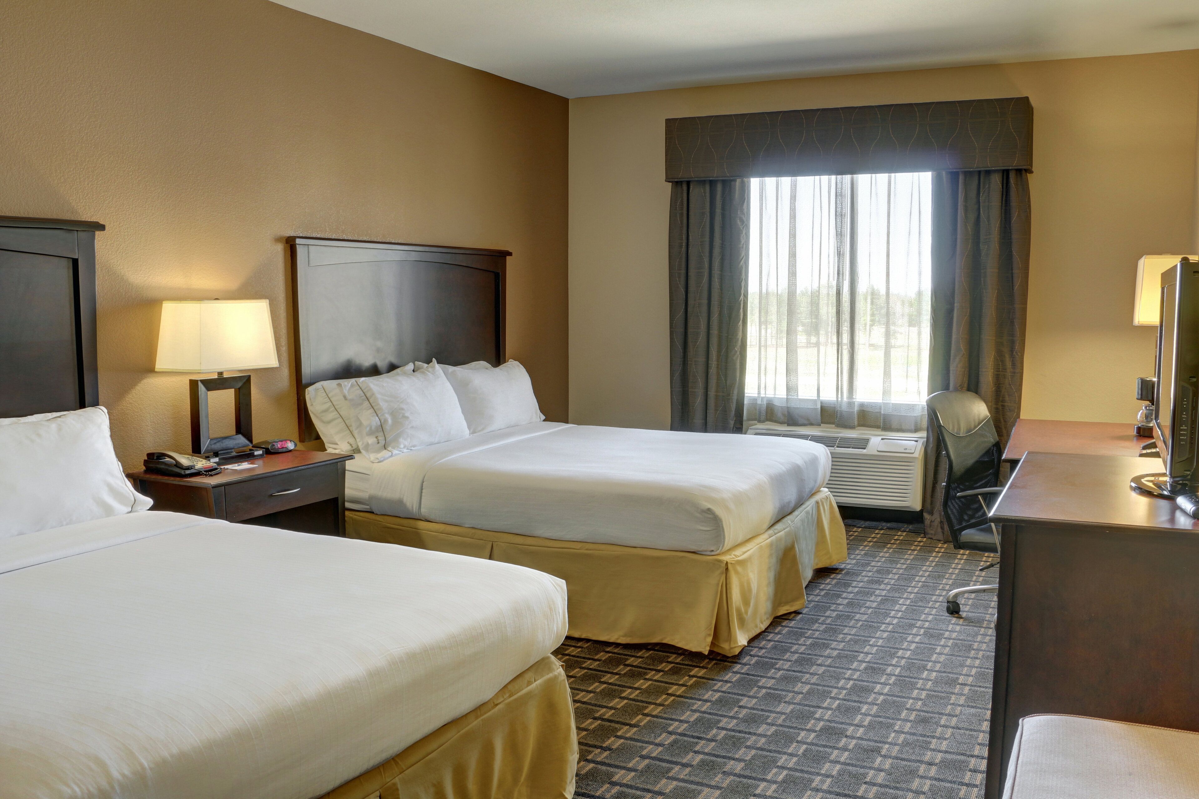 A hotel room with two beds, a desk, a chair, a lamp, and a window with curtains.