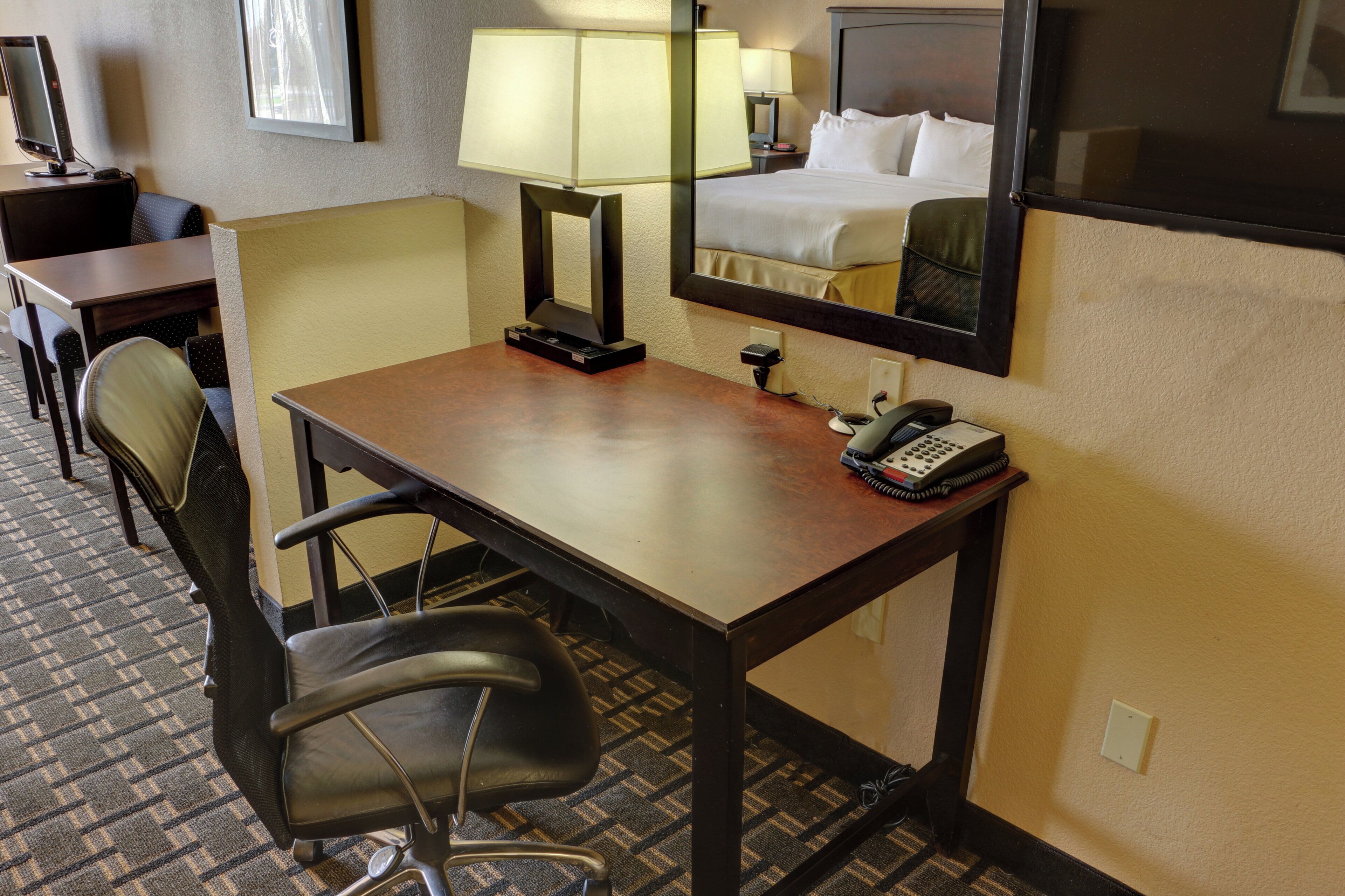 Una habitación de hotel con escritorio, silla, lámpara, teléfono y una cama con cabecera.