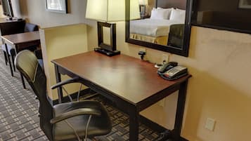Una habitación de hotel con escritorio, silla, lámpara, teléfono y una cama con cabecera.