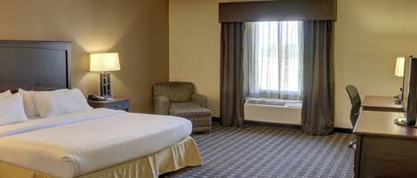 A hotel room with a large bed, a desk, a chair, and a window with curtains.