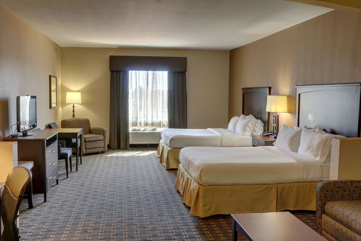 Een hotelkamer met twee bedden, een bureau met stoel, een televisietoestel en een raam met gordijnen.