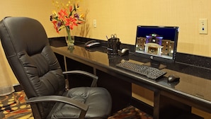 A hotel reception desk with a computer, a telephone, and a vase of flowers.