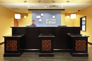 A hotel reception desk with a Holiday Inn Express sign, a priority check-in sign, and a security camera.