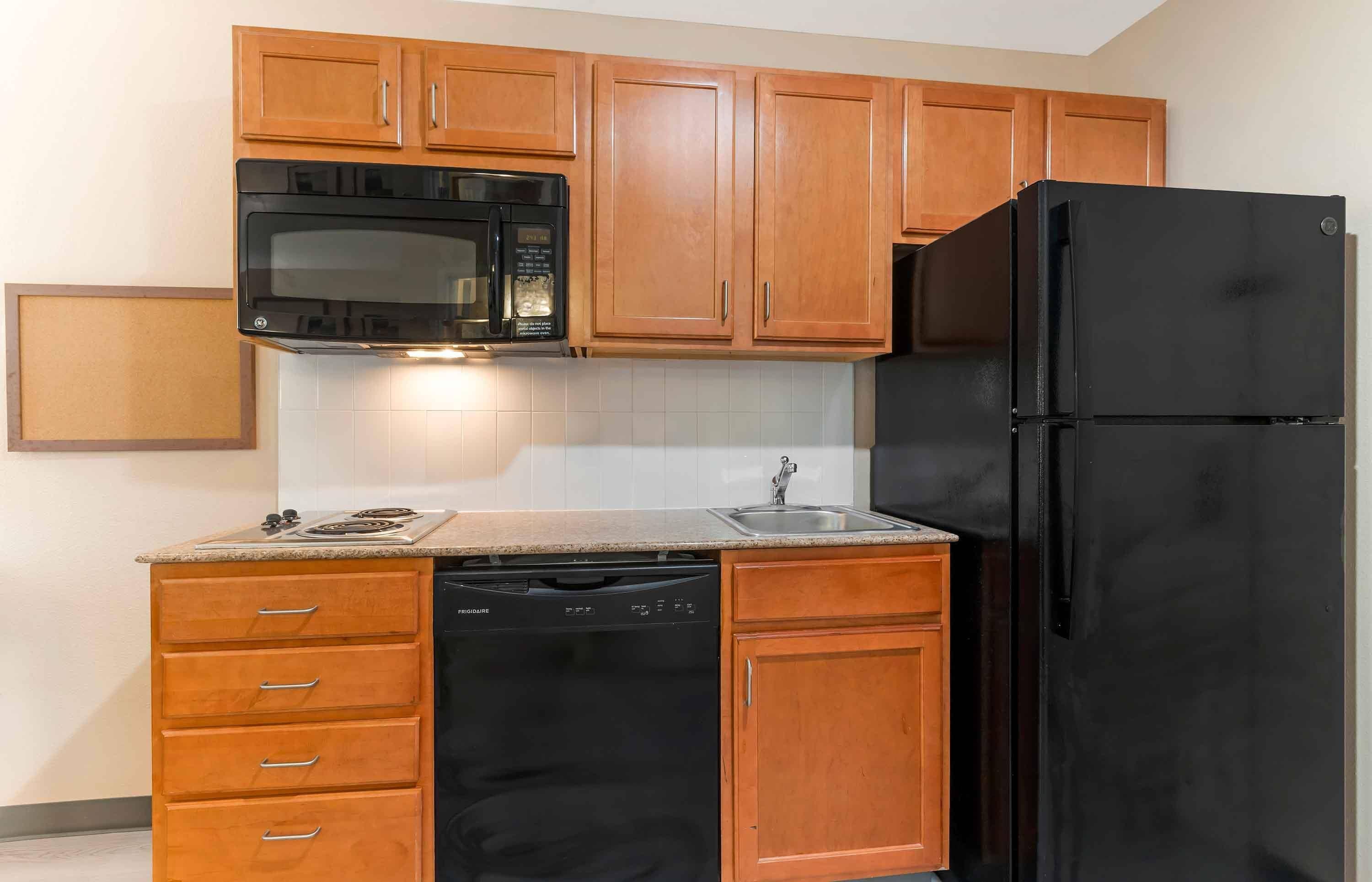 Una cocina con armarios de madera, un microondas negro, un refrigerador negro, un lavavajillas y una encimera de granito.