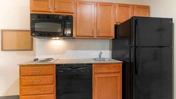 Una cocina con armarios de madera, un microondas negro, un refrigerador negro, un lavavajillas y una encimera de granito.