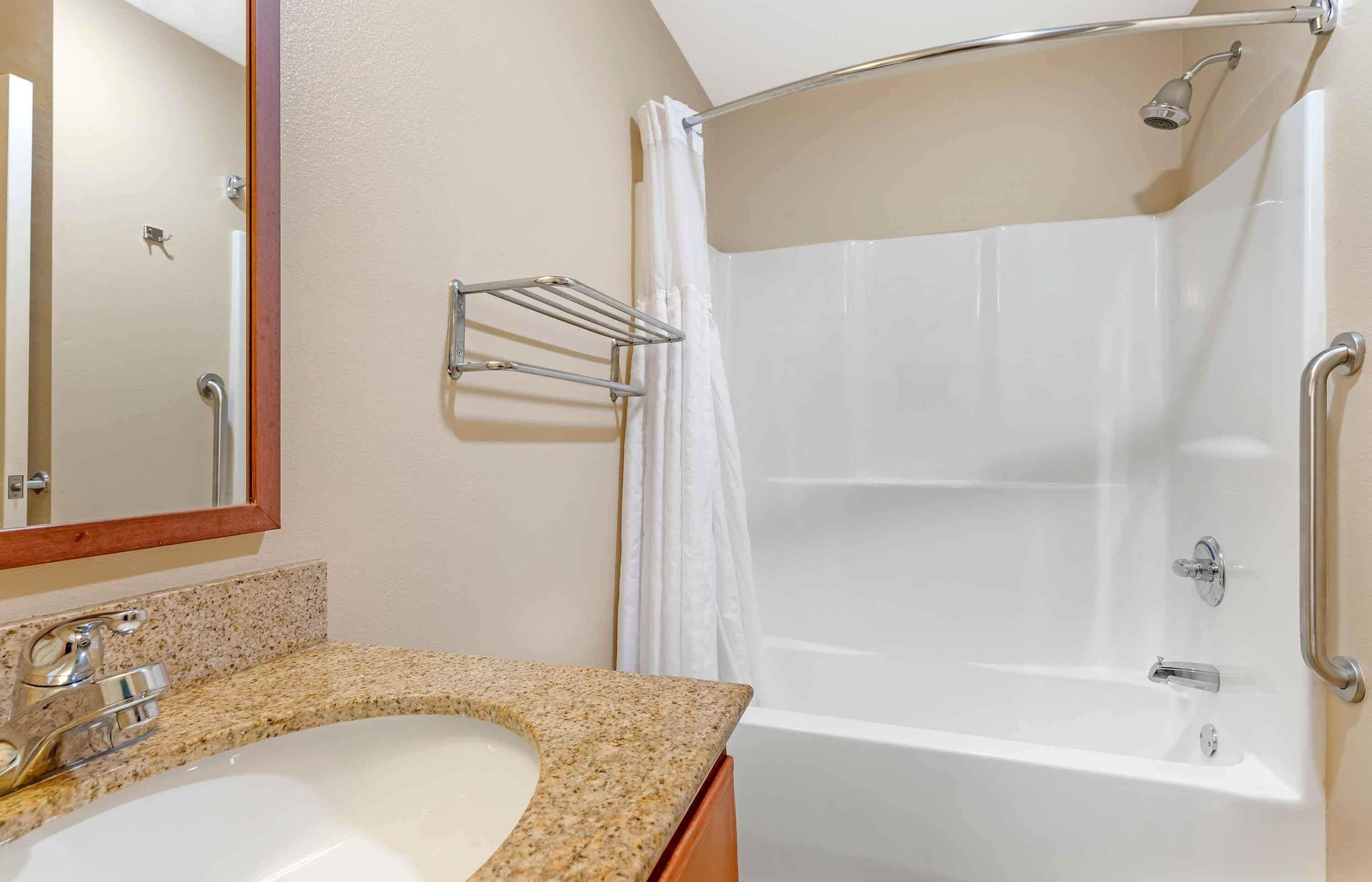 A bathroom with a sink, mirror, shower, and towel rack.