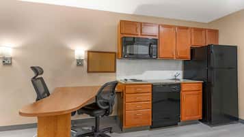 A compact kitchen with wooden cabinets, a black microwave, a black refrigerator, and a dining area with a wooden table and black office chair.