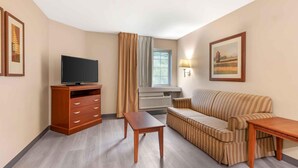 Habitación de hotel con un mueble bajo de madera para el televisor, un sofá a rayas, una mesita de madera pequeña y una ventana con cortinas.
