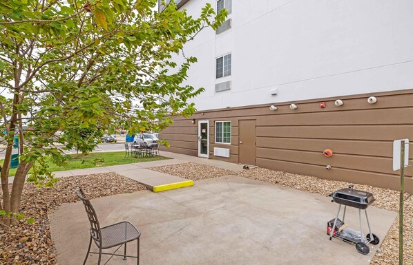 Un área de patio exterior con una parrilla, una silla de metal y una pequeña mesa.