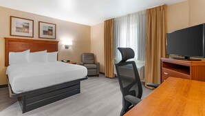 Una habitación de hotel con cama, escritorio, silla, televisor y cortinas.