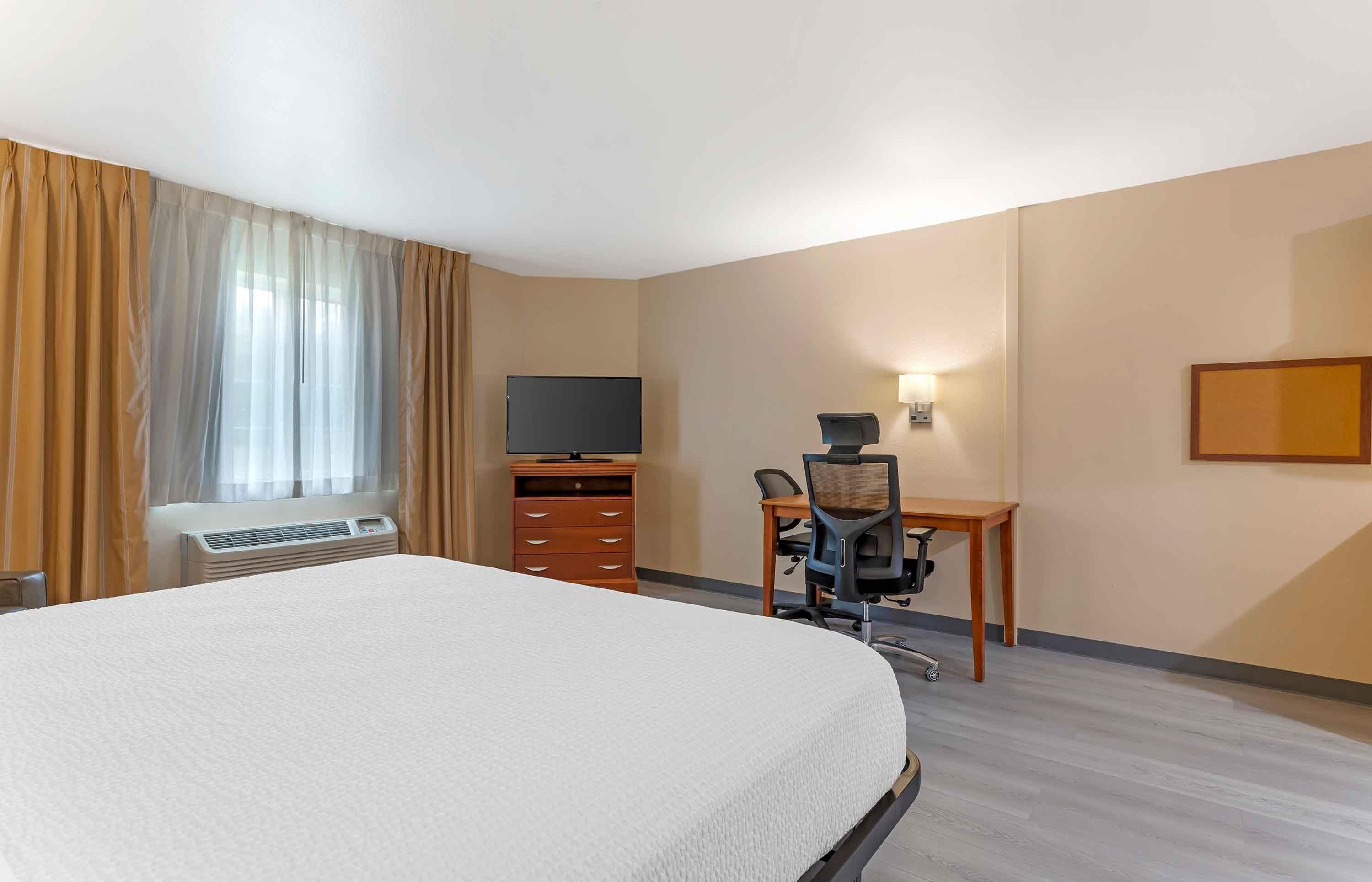 Habitación de hotel con una cama grande, un escritorio con silla, televisión, cómoda y ventana con cortinas.