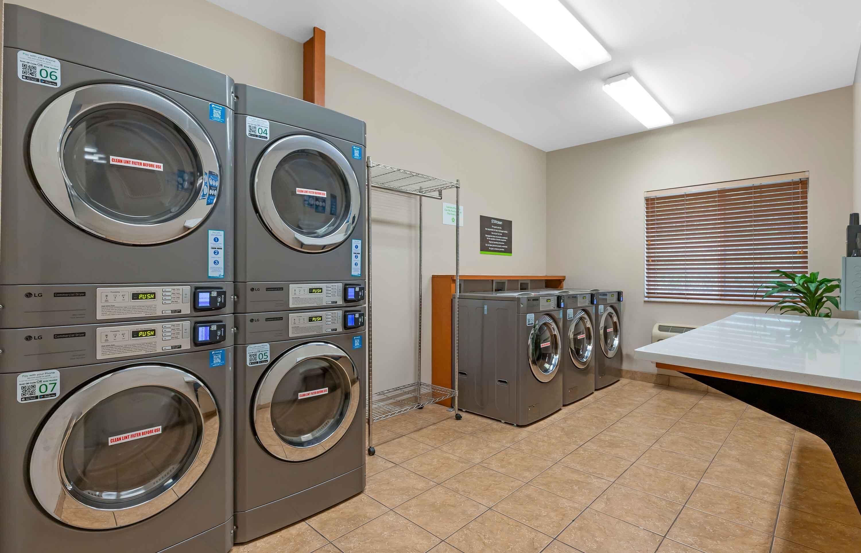 A laundry facility with multiple LG commercial dryers, a metal rack, and a tiled floor.