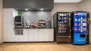 Una kitchenette con cafetera, refrigerador y máquina expendedora de Pepsi.