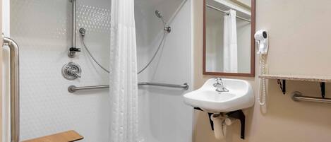 Un baño con ducha a nivel, barras de apoyo, un lavamanos blanco, un espejo y un perchero para toallas.