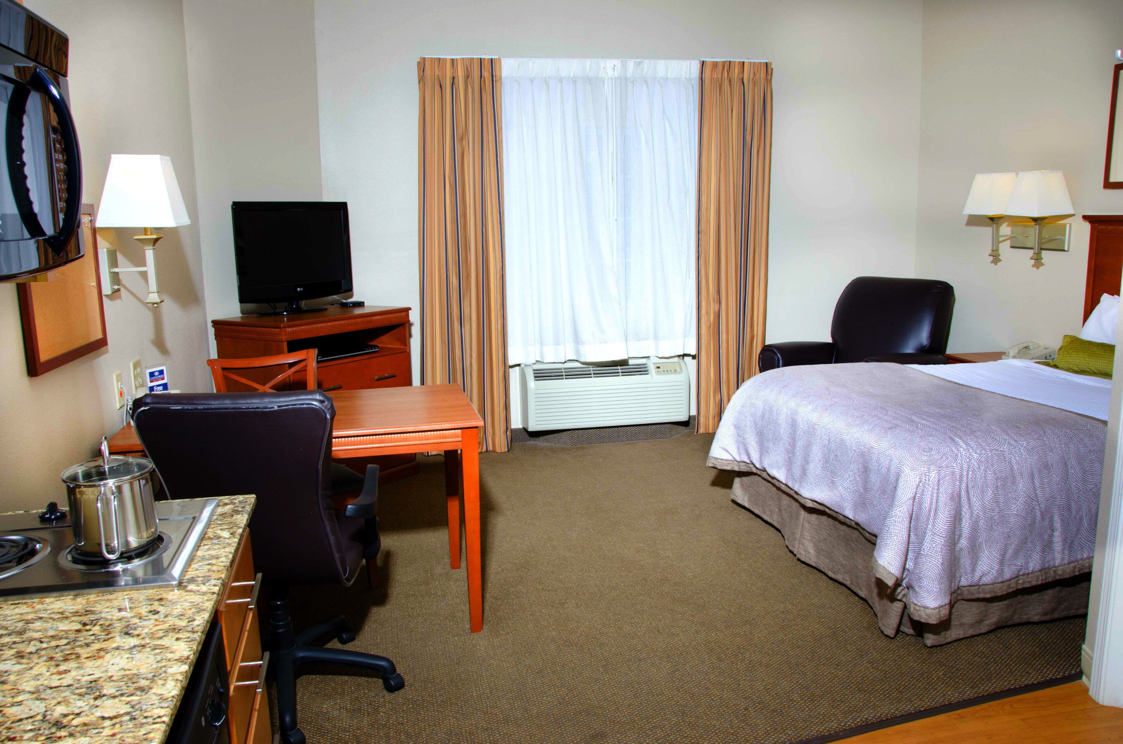 A hotel room with a bed, desk, chair, television, and a window with curtains.