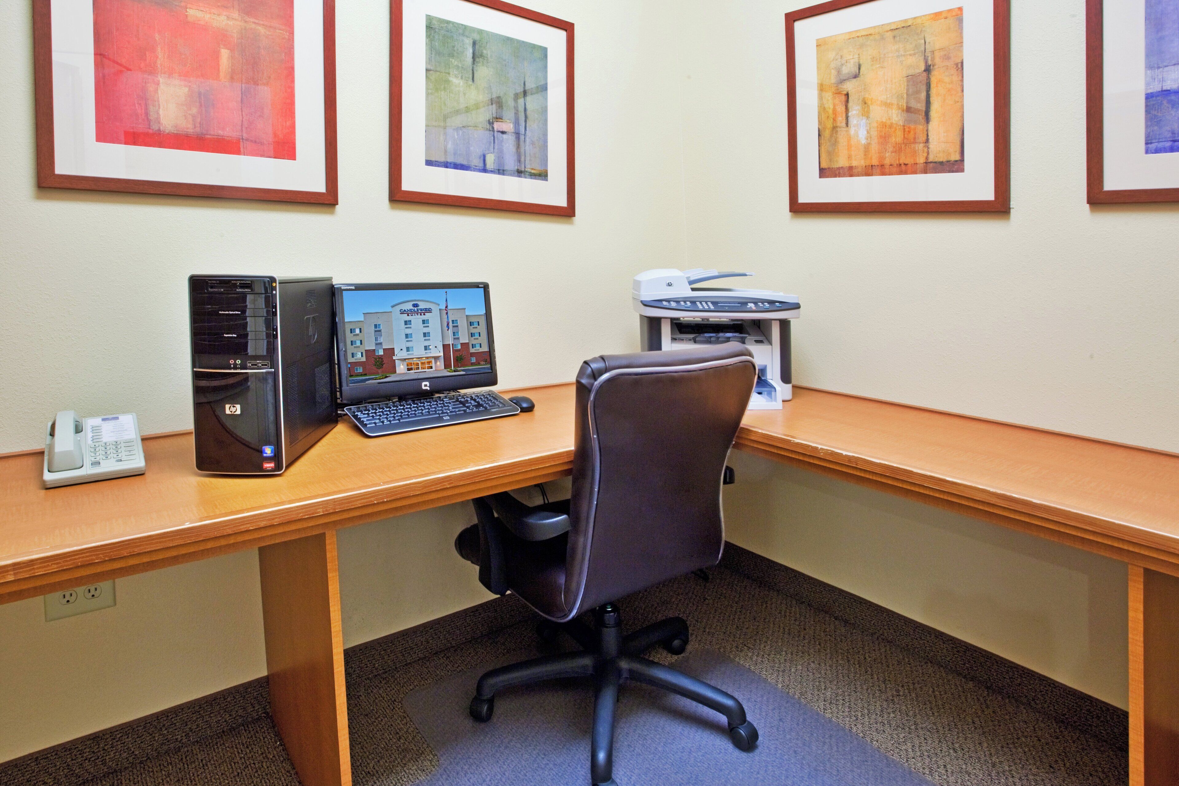 Un bureau d’hôtel équipé d’un ordinateur de bureau, d’une imprimante et d’œuvres d’art encadrées accrochées au mur.