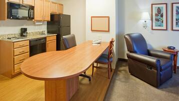 A compact kitchen with a microwave, refrigerator, and coffee maker. There is a dining table with chairs and a sofa.