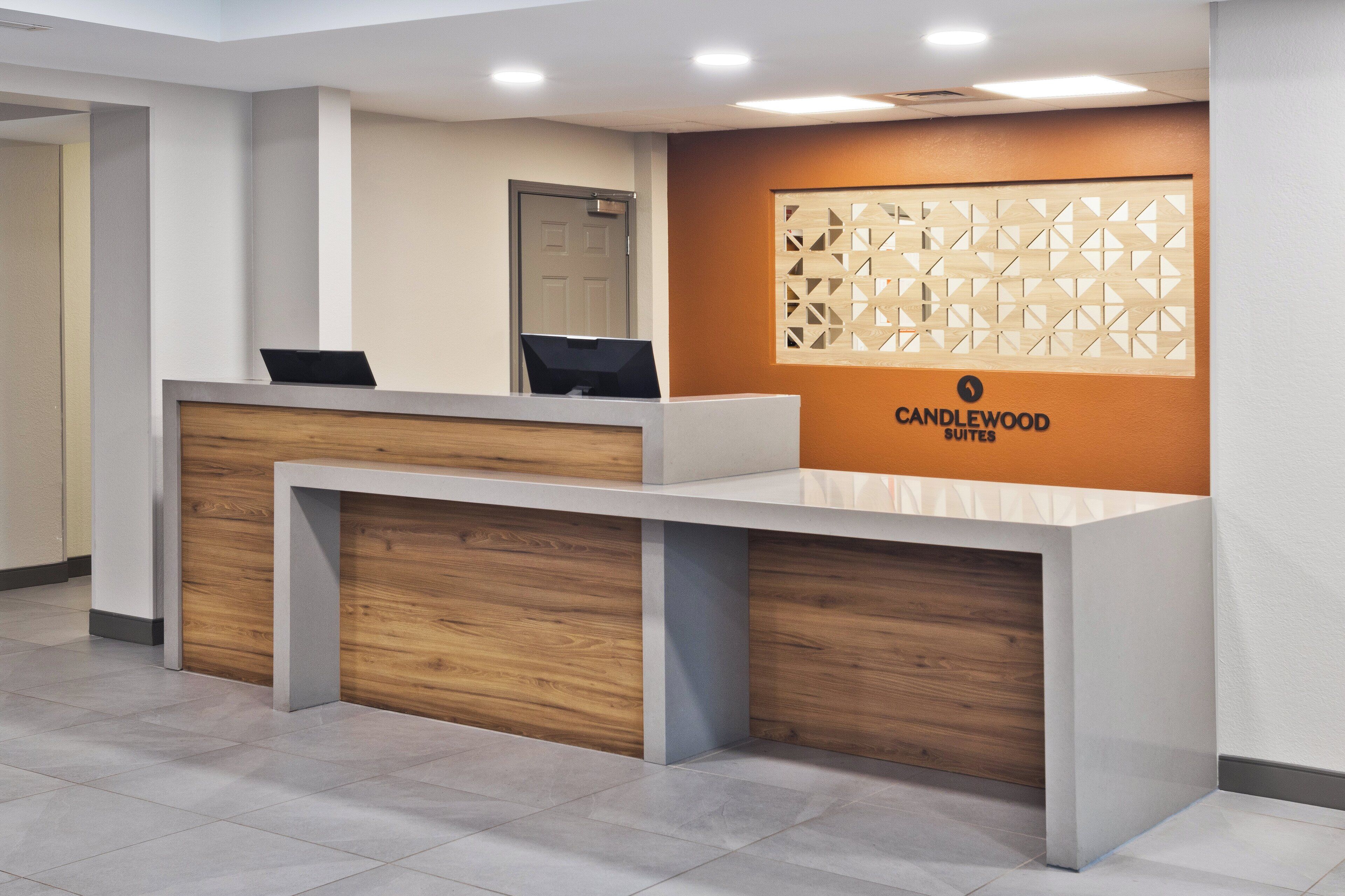 A reception desk with a modern design, featuring a wooden accent and a logo for Candlewood Suites.