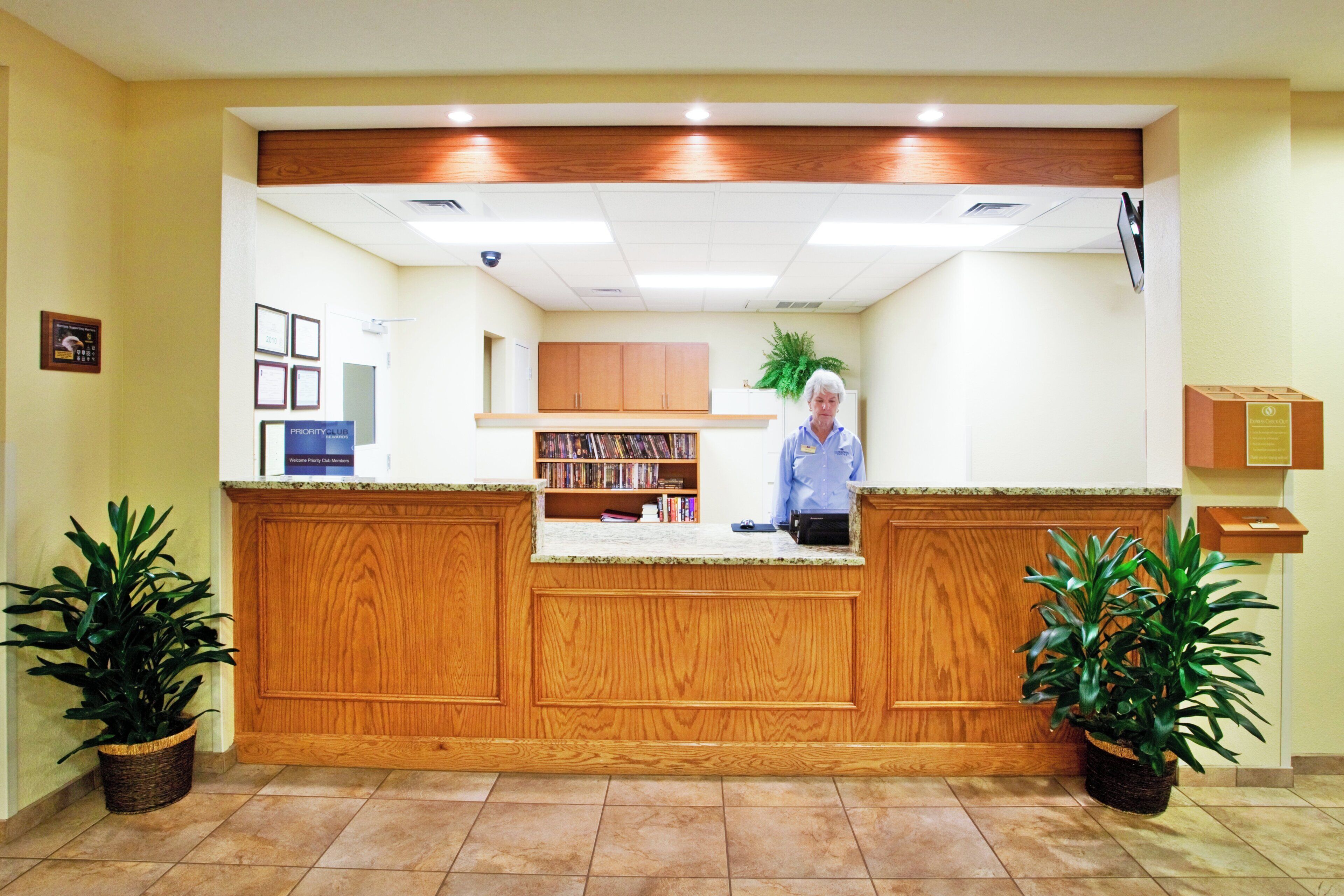 A reception desk with a wooden finish, a receptionist, and a bookshelf with books.