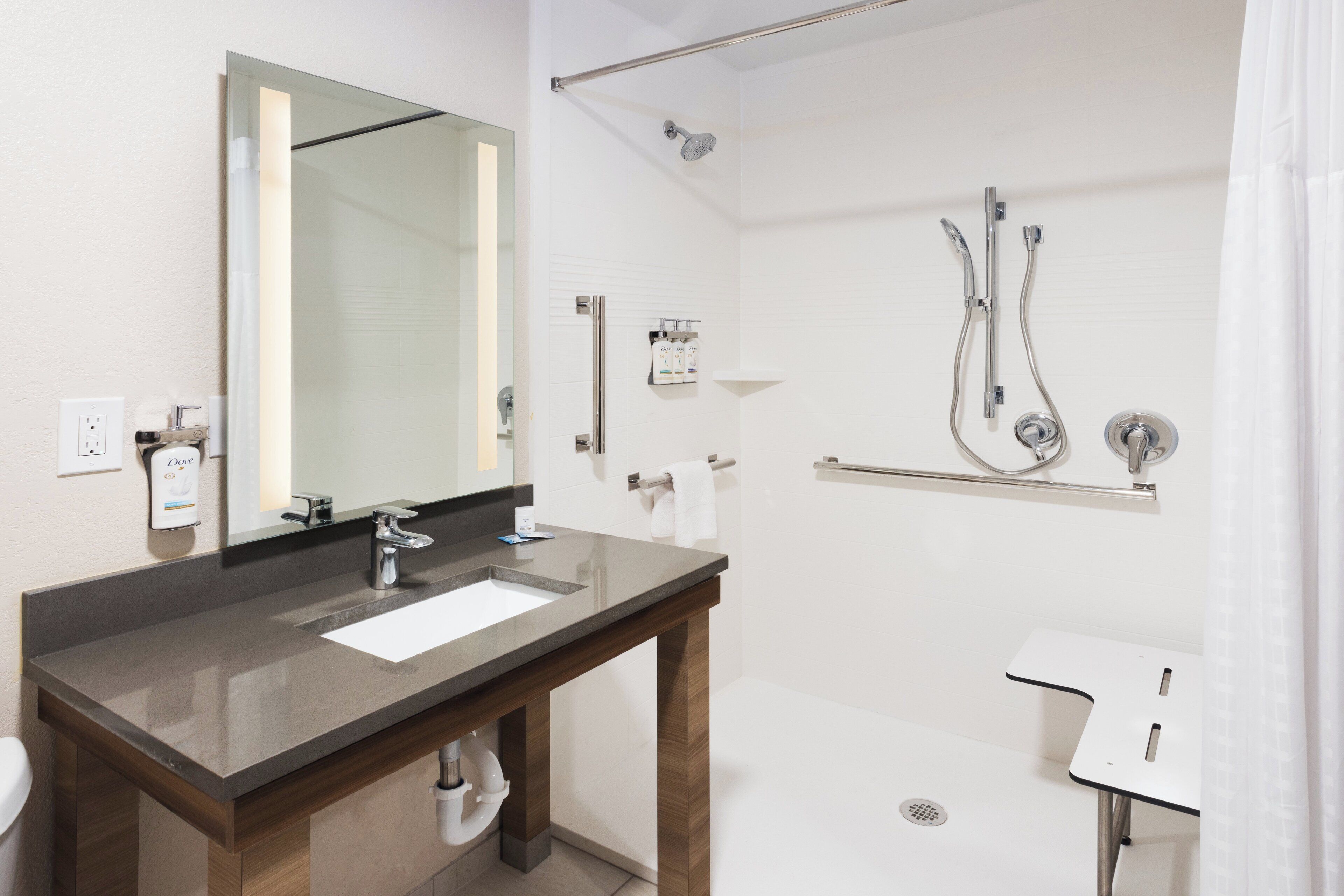 Un baño moderno con un espejo grande, un lavabo, una ducha con cabezal de ducha manual y un perchero para toallas.