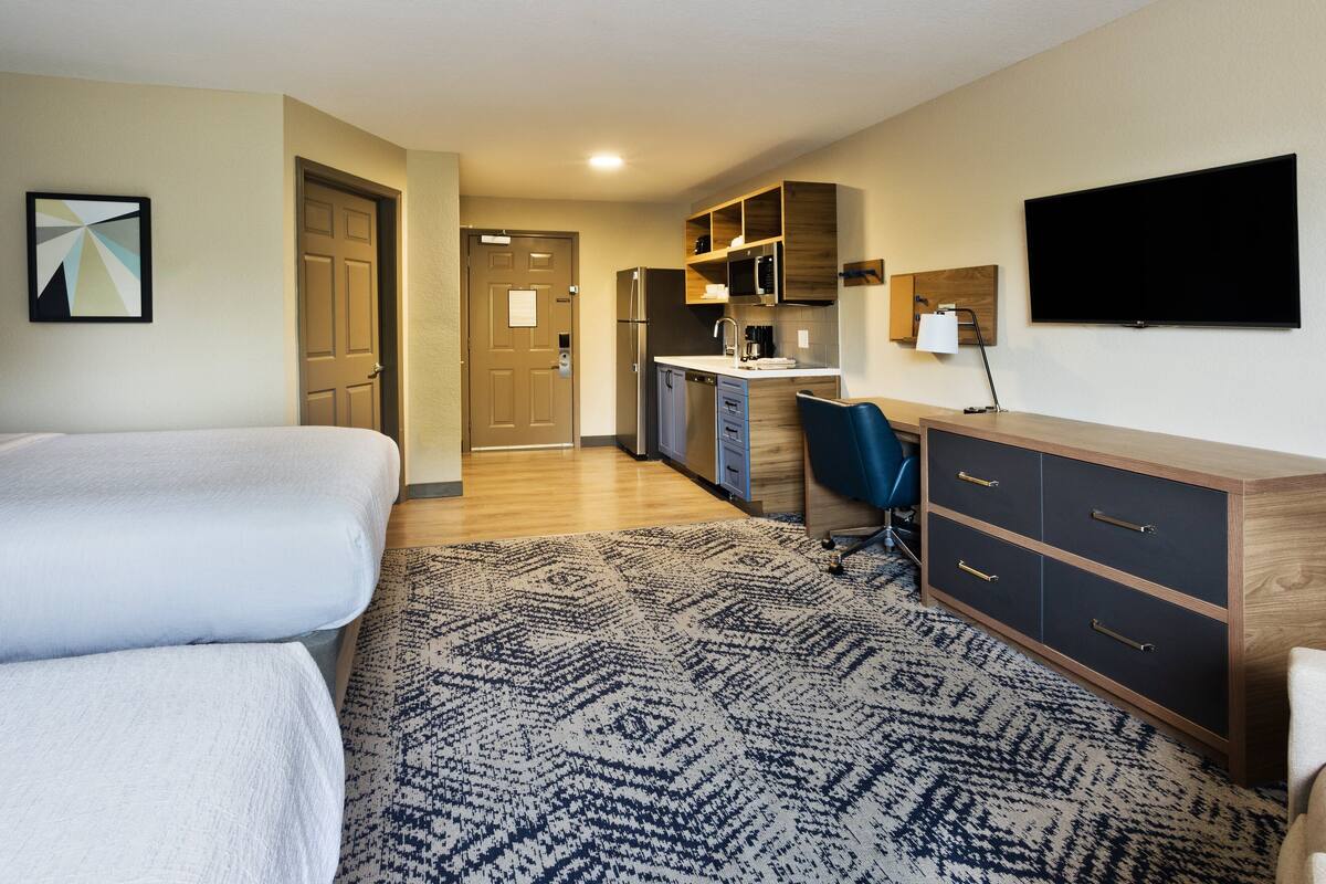 Ein Hotelzimmer mit Bett, Schreibtisch, Küchenzeile und Fernseher.