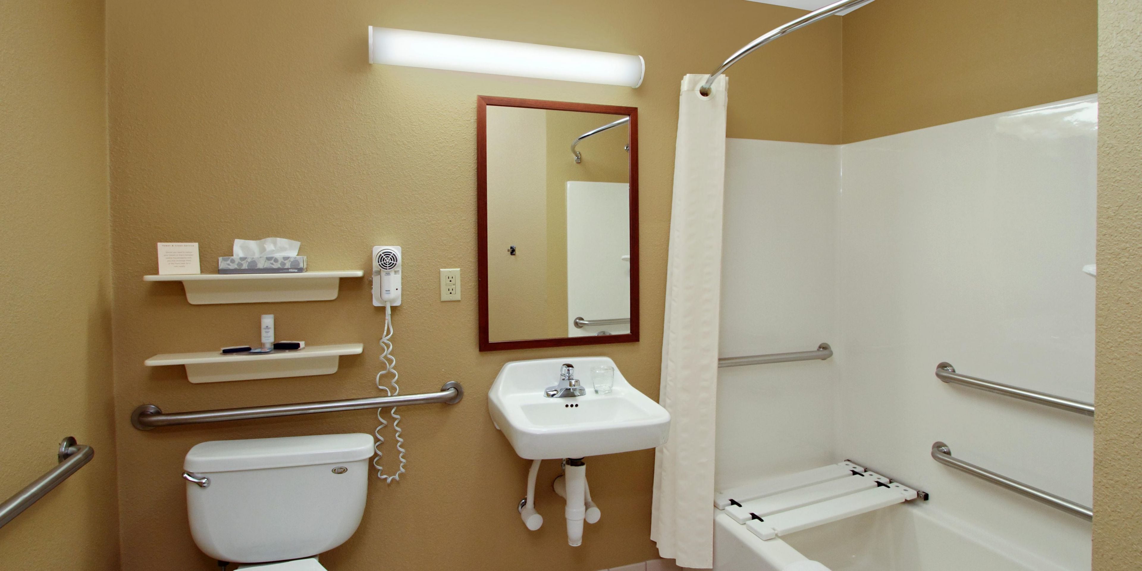 A bathroom with a toilet, sink, and shower. There are handrails and a mirror.
