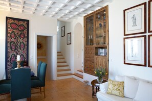 Um quarto com escada, sala de jantar com cadeiras e mesa, sofá com almofadas e um armário com portas de vidro.