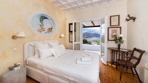 A bedroom with a bed, a round wall decoration, a table with a chair, and a view through an open door. - Villa Galaxy (Mykonos)