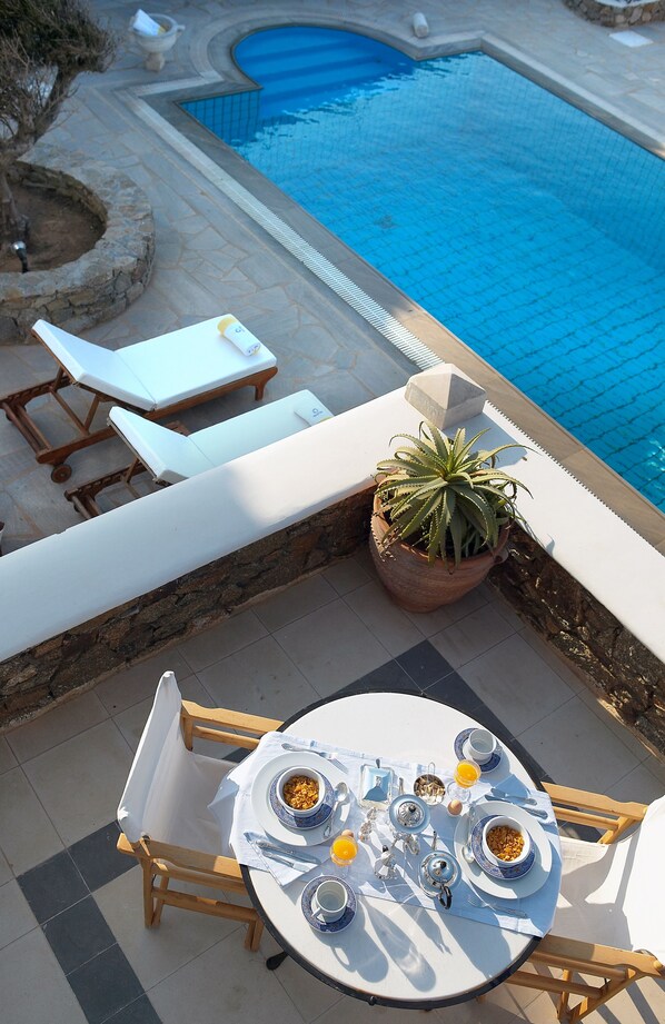 Zona de comedor junto a la piscina, con una mesa preparada para el desayuno y vistas a una piscina.