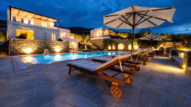 A modern poolside area with lounge chairs and umbrellas, stone walls, and a pool. - Villa Galaxy (Mykonos)