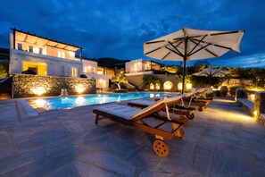 Un área moderna junto a la piscina con sillas de descanso y sombrillas, paredes de piedra y una piscina.