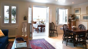 A dining area with a wooden table, chairs, and a view of the sea through open doors. - Villa Galaxy (Mykonos)