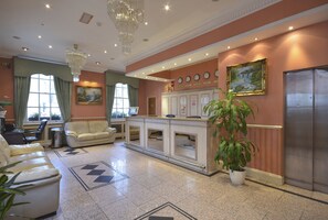 A hotel lobby with a reception desk, seating area, and a large potted plant. - Viking (London)