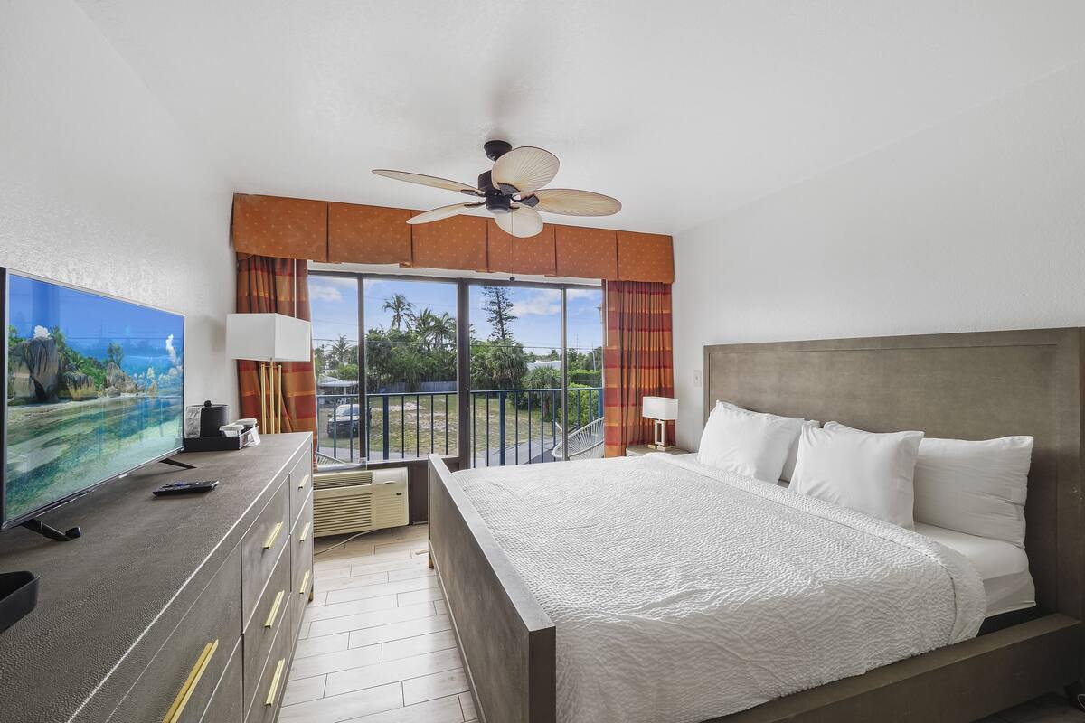 A hotel room with a large bed, a television, a ceiling fan, and a view of the outdoors.