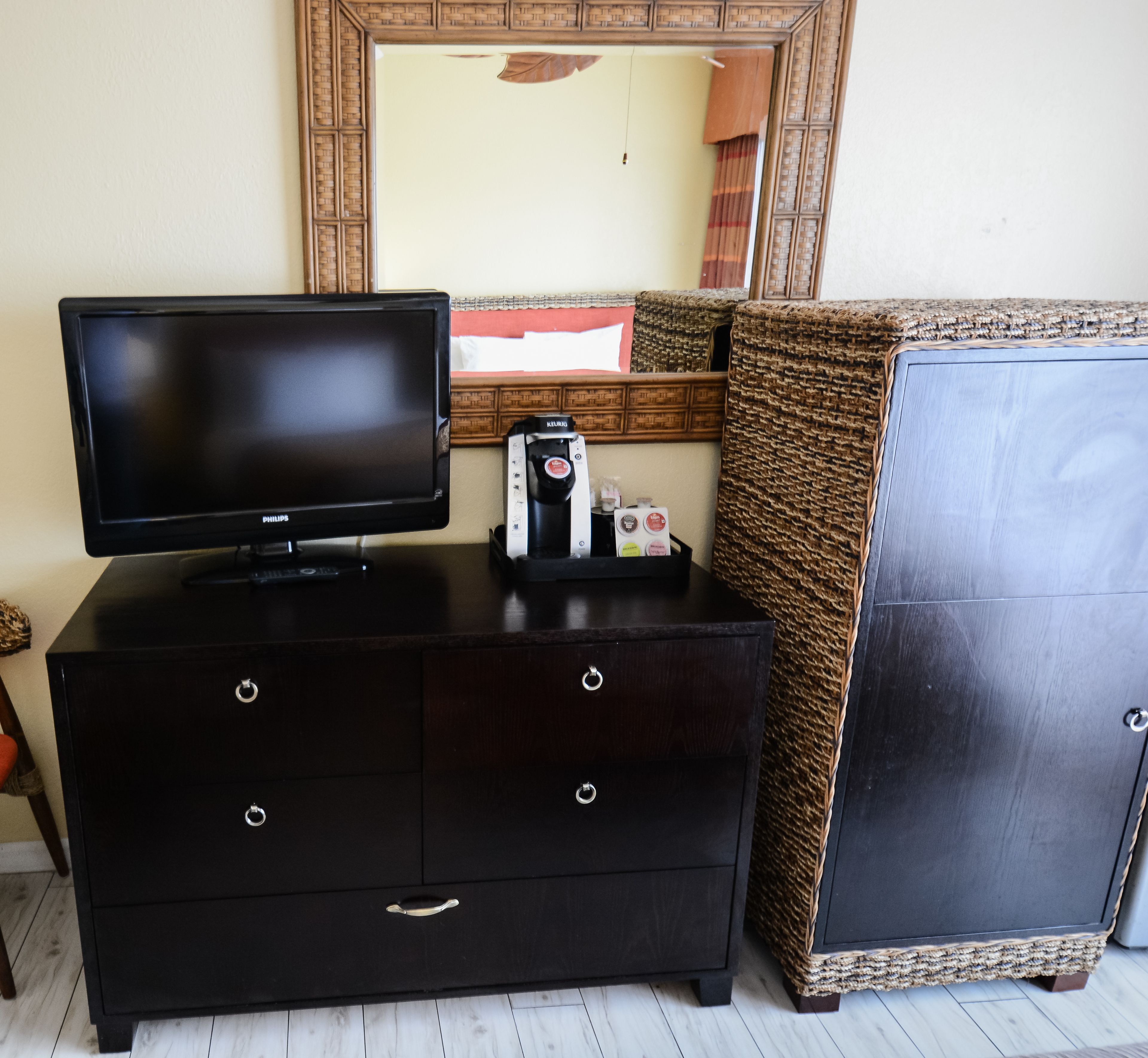 A black TV on a wooden dresser, a coffee maker, and a woven basket beside a cabinet.