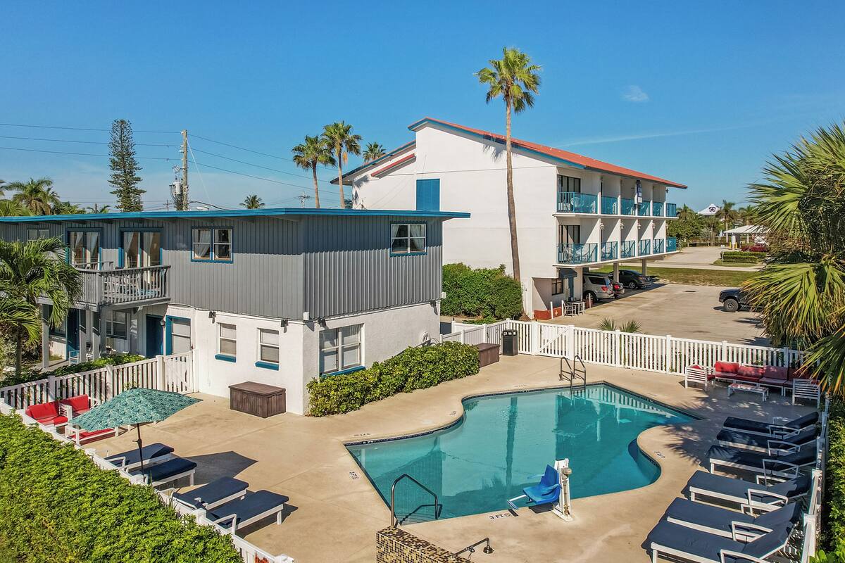 A resort with a swimming pool, lounge chairs, and a two-story building with balconies.