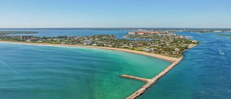 Ein Luftbild eines Küstenresorts mit einer langen Pier, die sich in das türkisfarbene Wasser erstreckt, umgeben von üppiger Vegetation und Strandhäusern.